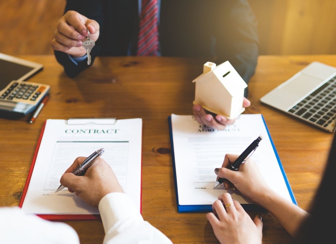 two people signing documents across the desk from a property manager handing them a key